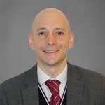 Das lvh-Team Porträt eines lächelnden Mannes in Anzug und roter Krawatte vor grauem Hintergrund