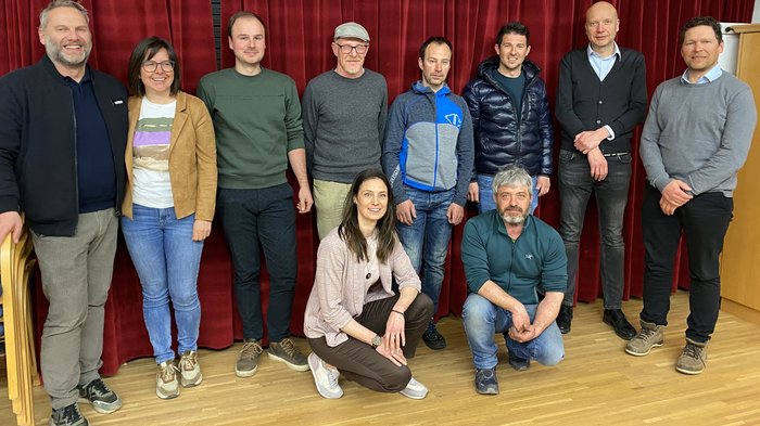 Riunione del gruppo comunale di lvh.apa: Artigianato, innovazione e prospettive future Foto di gruppo di dieci persone davanti a una tenda rossa in interno