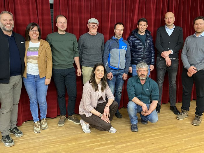 Riunione del gruppo comunale di lvh.apa: Artigianato, innovazione e prospettive future Foto di gruppo di dieci persone davanti a una tenda rossa in interno