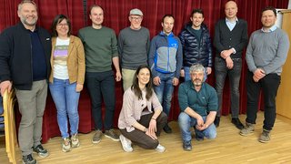 News Gruppenfoto von zehn Personen vor rotem Vorhang in Innenraum