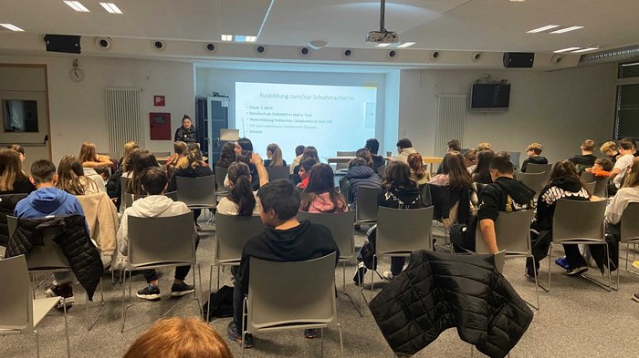 Mittelschule Klausen: Traumberufe in Gastgewerbe, Handwerk, Handel und Dienstleistungen vorgestellt Schulklasse hört zu bei einer Präsentation über Schuster-Ausbildung in einem Klassenzimmer.