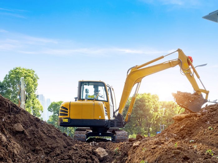 Imprese movimento terra: tra appalti pubblici, mobilità e infrastrutture Escavatore giallo che solleva terra in un cantiere con alberi sullo sfondo