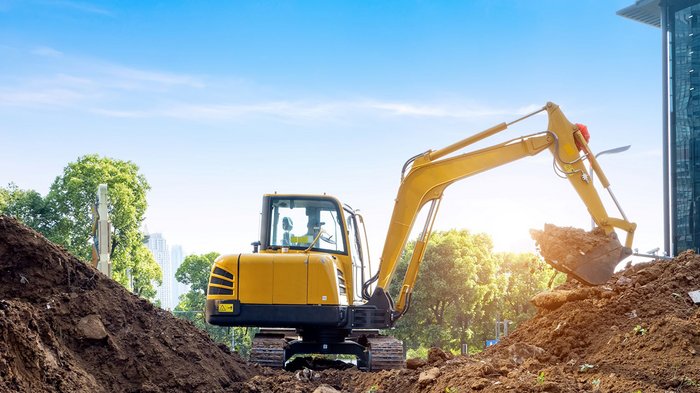 Tiefbauunternehmer: Öffentliche Aufträge, Mobilität und Infrastruktur Gelber Bagger hebt Erde auf einer Baustelle mit Bäumen im Hintergrund