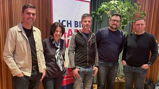 News Fünf Personen vor einem Banner und einer Pflanze in einem Raum