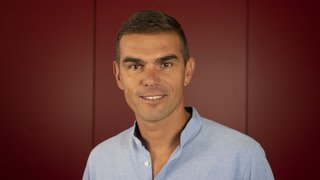 News Porträt eines lächelnden Mannes vor rotem Hintergrund