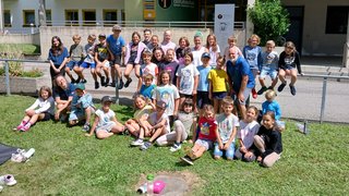 News Gruppenfoto von Kindern und einem Erwachsenen vor einer Berufsschule im Sonnenschein
