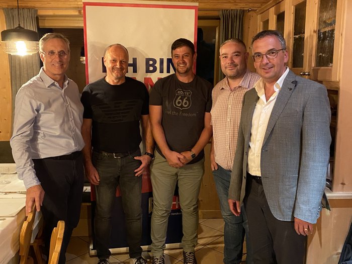 Neuer Handwerkerobmann in Schluderns Fünf Männer stehen in einem Holzraum vor einem Banner mit freundlichen Gesichtern