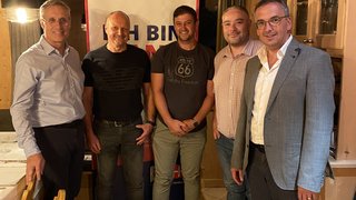 News Fünf Männer stehen in einem Holzraum vor einem Banner mit freundlichen Gesichtern