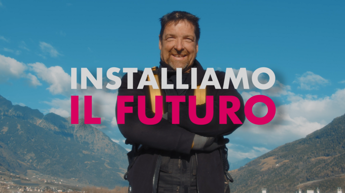 "La tutela del clima è lavoro e noi lo facciamo ogni giorno" Uomo sorridente davanti a paesaggio montano con cielo azzurro e testo Installiamo il futuro
