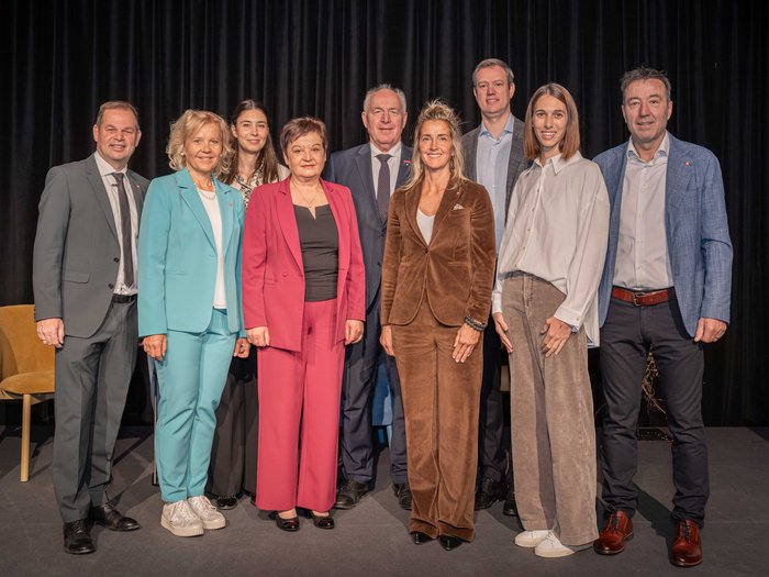 Wachstum im Gleichgewicht Neun Personen in Businesskleidung posieren vor schwarzem Vorhang auf Bühne