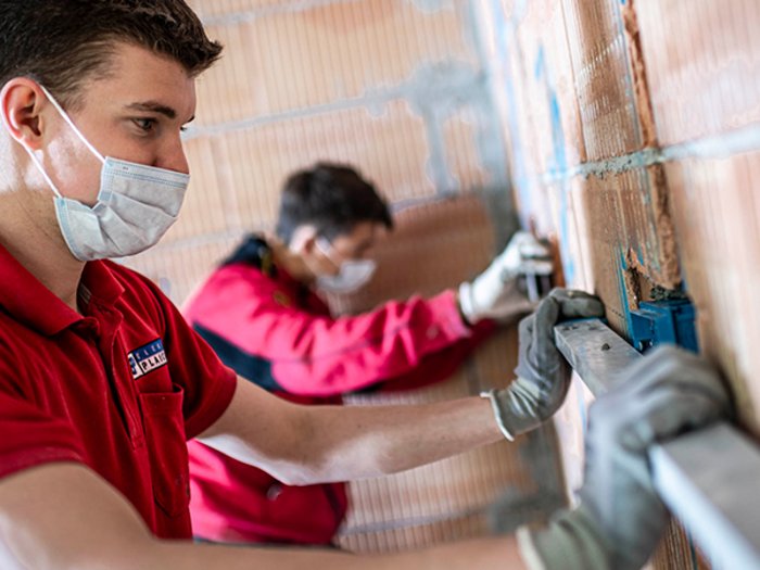 Haller: „Arbeit und Wirtschaftskreisläufe müssen aufrechterhalten bleiben“ Zwei Handwerker mit Masken, die an einer Wand in einem Rohbau arbeiten