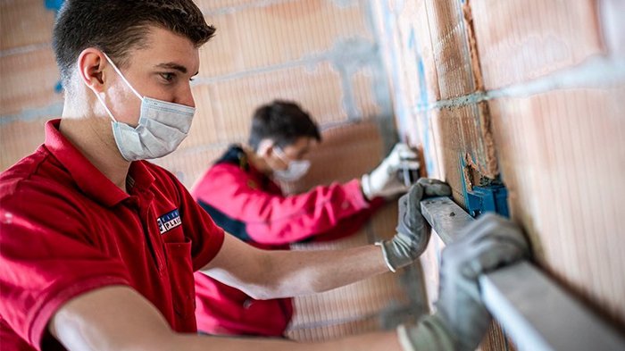 Haller: „Arbeit und Wirtschaftskreisläufe müssen aufrechterhalten bleiben“ Zwei Handwerker mit Masken, die an einer Wand in einem Rohbau arbeiten