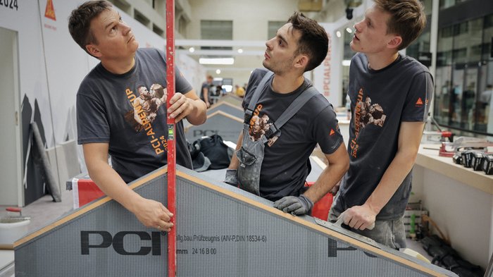 Südtirol begeistert beim Wettkampf der Fliesenleger/innen in Bozen! Drei Männer bei Bauarbeit mit Wasserwaage und Schrägelement beim PCI Alpen Cup 2024