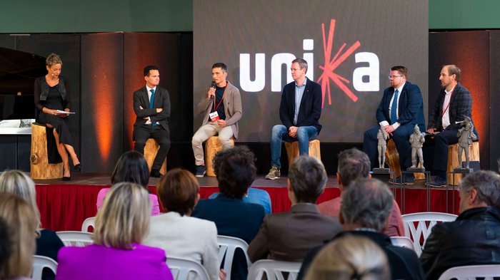 La 31^ Fiera d’Arte UNIKA apre le porte a Ortisei Panel di sei persone in discussione davanti al pubblico con logo Unia sullo sfondo