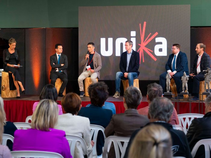 La 31^ Fiera d’Arte UNIKA apre le porte a Ortisei Panel di sei persone in discussione davanti al pubblico con logo Unia sullo sfondo