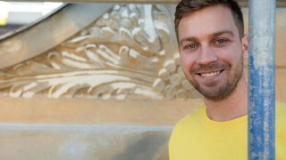 News Lächelnder Mann in gelbem Shirt vor dekorativer Wand