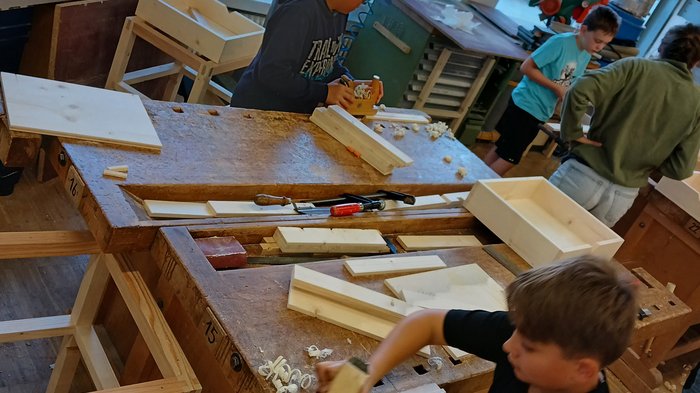 Mit Holz, Wasser & Handwerksfreude: Die KidsAcademy ist in Bruneck angekommen Kinder bearbeiten Holzstücke in einer Werkstatt an Holzbänken.