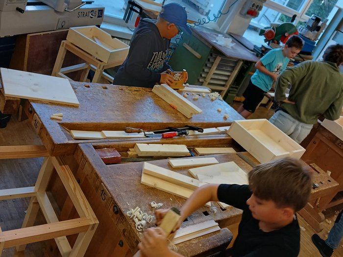 Mit Holz, Wasser & Handwerksfreude: Die KidsAcademy ist in Bruneck angekommen Kinder bearbeiten Holzstücke in einer Werkstatt an Holzbänken.