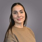 Ines Girardi Ritratto di giovane donna con maglione marrone su sfondo grigio