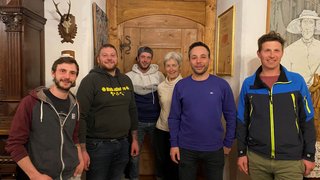 News Sechs Personen stehen vor einer Holztür in einem gemütlichen Raum