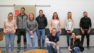 News Gruppe von neun jungen Erwachsenen, die in einem hellen Raum lächelnd posieren