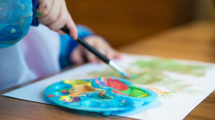 Familienfreundliche Berufswelt Kind malt mit Wasserfarben und Pinsel auf Papier