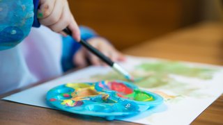 News Kind malt mit Wasserfarben und Pinsel auf Papier