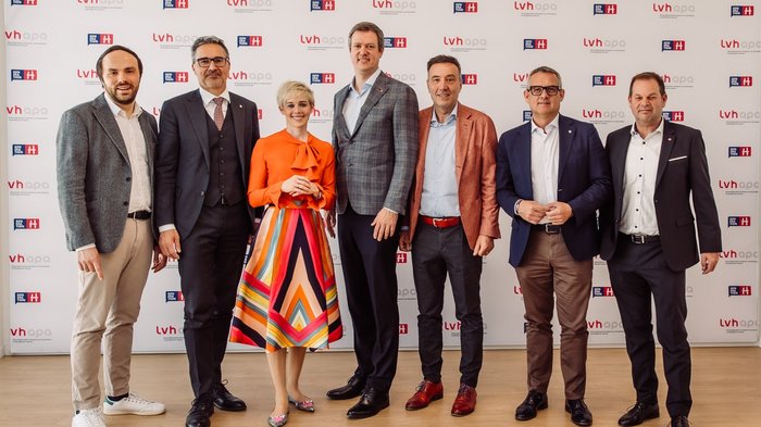 Consumo di suolo record in Italia - continua l’aumento anche in Alto Adige Sette persone in abbigliamento formale davanti a muro pubblicitario lvh apa