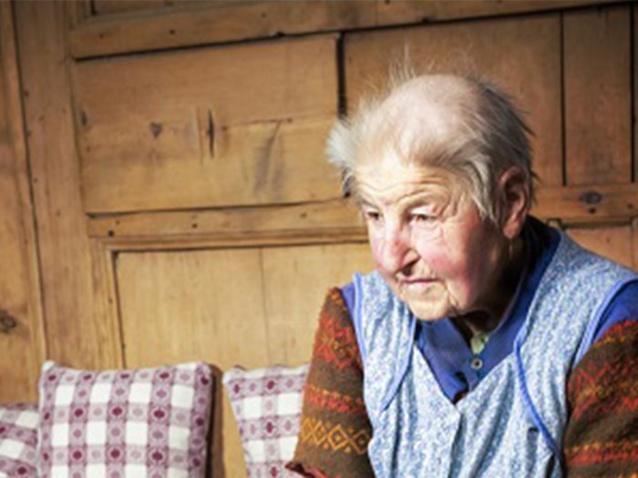 „Nicht den Mut verlieren“ Ältere Frau mit traditioneller Kleidung sitzt auf einem Sofa vor Holzwand