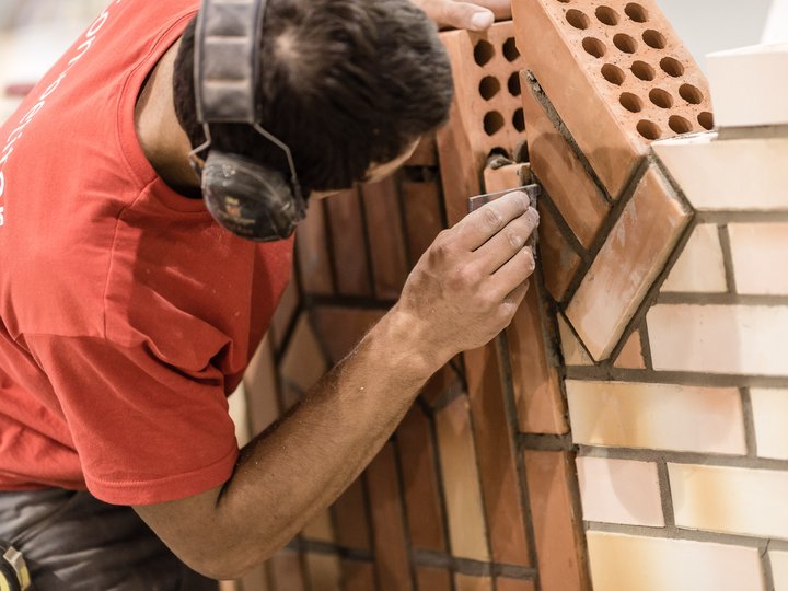 Baumeister und Maurer Maurer verputzt Ziegelwand mit Schleifpapier