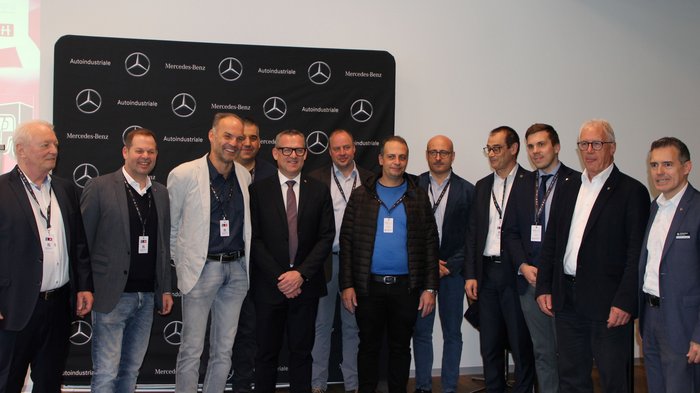 Warentransporteurinnen und -transporteure: Zukunftsvision und aktuelle Herausforderungen Gruppe von zwölf Männern steht vor Mercedes-Benz und Autoindustriale Hintergrund