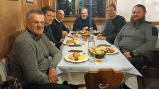 News Sechs Männer sitzen an einem Tisch mit Speisen und Getränken in einem gemütlichen Raum