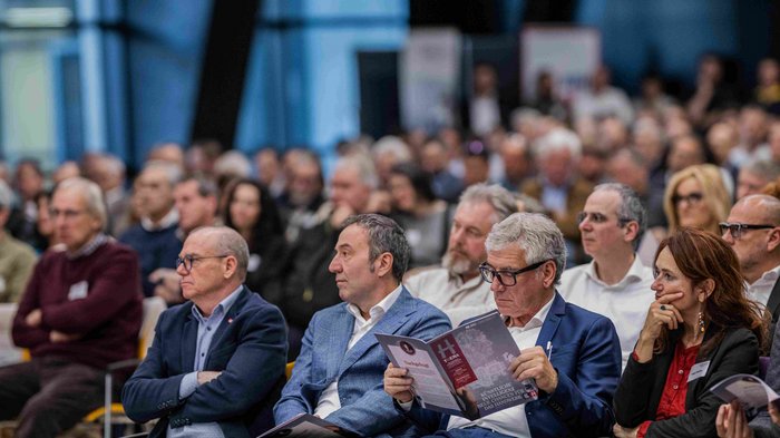Intelligenza artigiana: nuove opportunità grazie all‘IA Pubblico a una conferenza legge il programma e ascolta attentamente