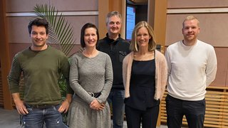 News Fünf Personen stehen nebeneinander in einem Innenraum und lächeln in die Kamera