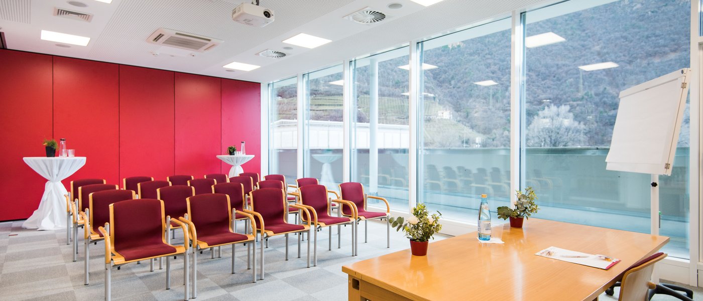Vermietung Seminarräume Konferenzraum mit roten Stühlen, großem Fenster und Flipchart