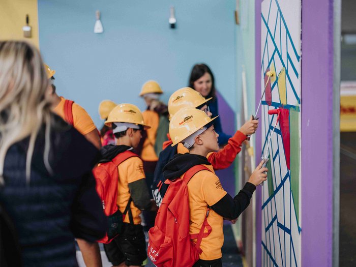 L‘iniziativa "Abenteuer Handwerk" (“Avventura Artigianato”) appassiona le giovani generazioni ai mestieri artigianali in Val Pusteria Bambini con caschi da cantiere dipingono un muro durante un'attività di gruppo