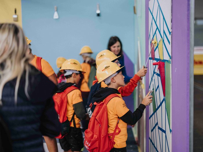"Abenteuer Handwerk" - Initiative begeistert junge Generation für Handwerksberufe im Pustertal Kinder mit Bauhelmen malen eine Wand während einer Gruppenaktivität