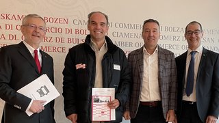 News Vier lächelnde Männer in formeller und legerer Kleidung vor einer Handelskammer-Wand.