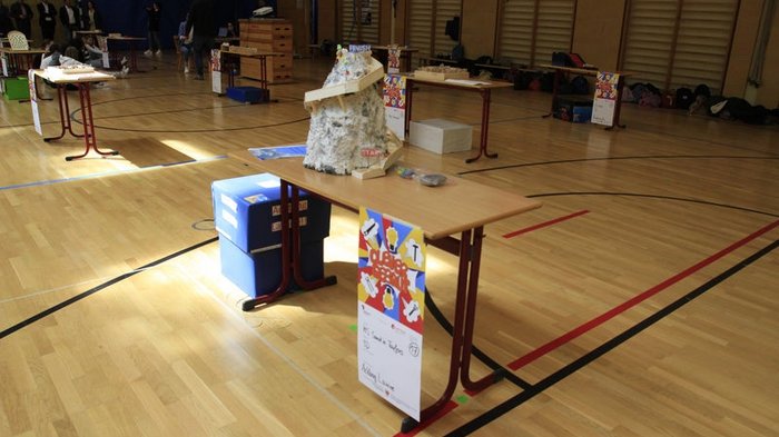 Kreative Spielideen: Preisverleihung für "Clever gebaut" Modell auf Tisch in Turnhalle mit Personen im Hintergrund