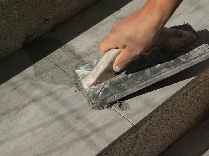 Fliesen-, Platten- und Mosaikleger Hand glättet Beton auf Treppenstufe mit Glättkelle