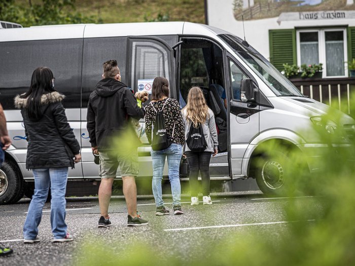 Il consorzio CAA prende posizione sull’esclusione dalla gara pubblica Persone in fila con mascherine che salgono su un minibus