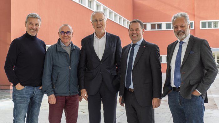 Lvh.apa ed Eurac Research: cooperazione all’insegna della sostenibilità Cinque uomini sorridenti davanti a un edificio rosso all'aperto