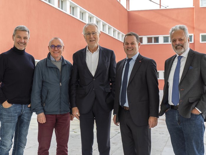 Lvh.apa ed Eurac Research: cooperazione all’insegna della sostenibilità Cinque uomini sorridenti davanti a un edificio rosso all'aperto