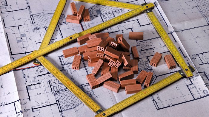 © Fresnel/Shutterstock.com Architektonischer Bauplan mit Miniaturziegeln und gelbem Maßband