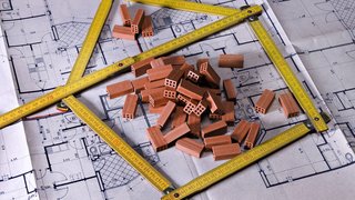 © Fresnel/Shutterstock.com Architektonischer Bauplan mit Miniaturziegeln und gelbem Maßband