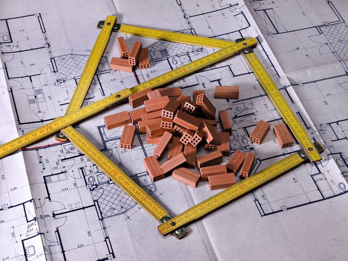 © Fresnel/Shutterstock.com Architektonischer Bauplan mit Miniaturziegeln und gelbem Maßband