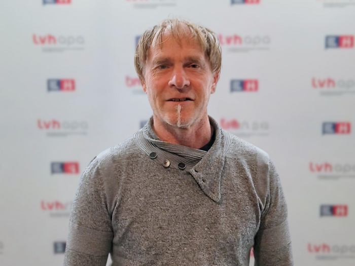 Due funzionari volenterosi assumono nuovi incarichi Uomo con maglione grigio davanti a fondo pubblicitario TVH Apa