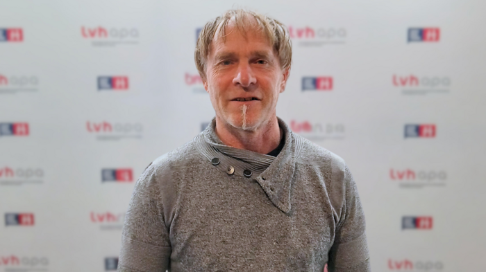 Due funzionari volenterosi assumono nuovi incarichi Uomo con maglione grigio davanti a fondo pubblicitario TVH Apa