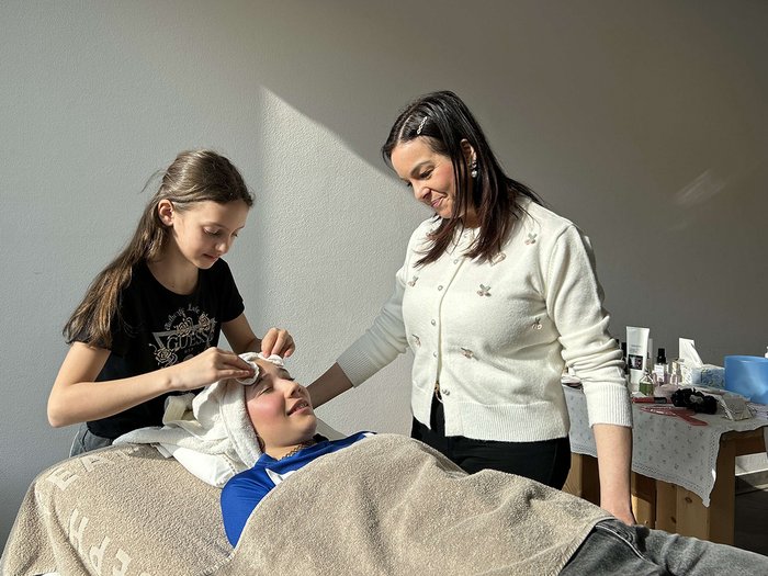 40 Betriebe, 100 Jugendliche, 15 Berufe Mädchen bekommt Gesichtsbehandlung von zwei anderen Frauen in hellem Raum