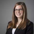 Arianne Schanung Ritratto di una donna sorridente con occhiali e capelli castani lunghi su sfondo grigio